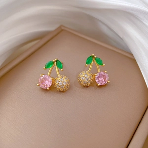 Macro shot of cherry-shaped gold earrings with pink crystals and green leaf stones