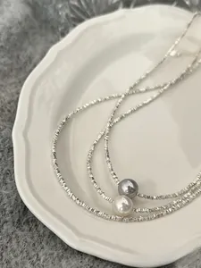 Detail of S925 silver beaded necklace with white and grey pearls on a ceramic plate