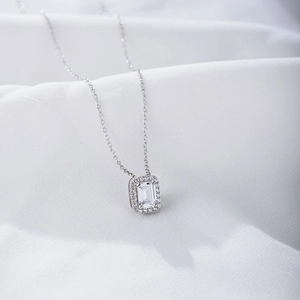 Detail of emerald cut zircon pendant on white satin with halo setting necklace