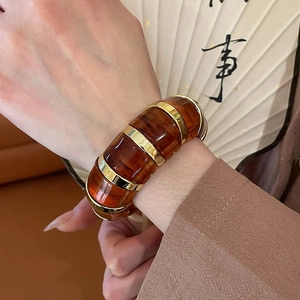 Detail of amber resin bangle with gold accents worn against a vintage fan background