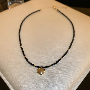 Vue détaillée des perles de cristal noir facettées et du pendentif en forme de cœur doré brillant