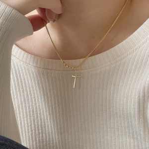 Close-up of minimalist golden cross pendant necklace worn over white knitted fabric