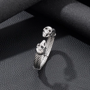 Detailed close-up of punk double skull steel wire bracelet on black leather surface