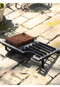 Macro shot of cast iron boot scraper with natural fiber bristles on a stone patio