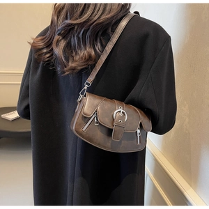 Close-up of brown leather saddle bag showing adjustable shoulder strap and side zipper detail