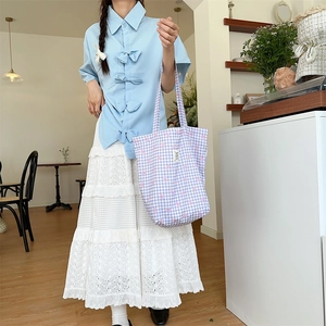 Detail view of a purple plaid tote bag paired with a lace skirt and blue shirt