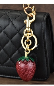 Close-up of a sparkling red sequin strawberry keychain with gold hardware on a black bag