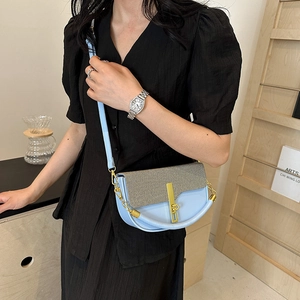 Blue crossbody bag with woven texture lid and golden hardware worn by a model in a cafe