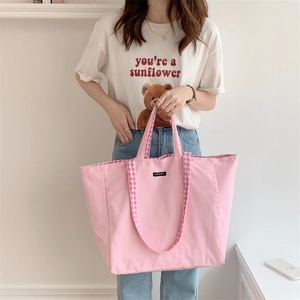 Pink canvas tote bag with checkered handles held by model in minimalist indoor setting