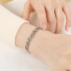 Close-up of silver chain bracelet with pink zircons worn on wrist with beige knit background