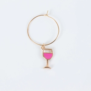 Detail of a golden hoop earring featuring a pink enamel wine glass charm on white background