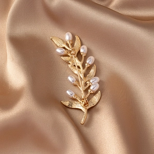Detail of vintage golden leaf brooch with white pearl on champagne satin background