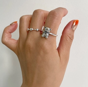 Close-up of minimalist 925 sterling silver teddy bear and heart chain rings worn on hand