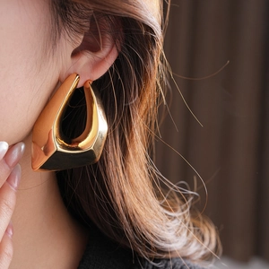 Close-up of a large chunky golden irregular geometric earring worn on a model ear