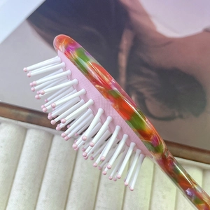 Detail view of a mini colorful acetate air cushion hairbrush on textured fabric background
