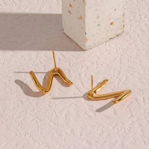 Detailed view of gold plated Z-shaped wavy stud earrings on a minimalist stone display