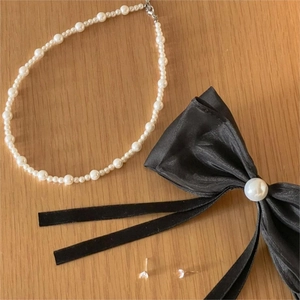Flat lay of a pearl necklace with a large black bow hair clip and silver stud earrings