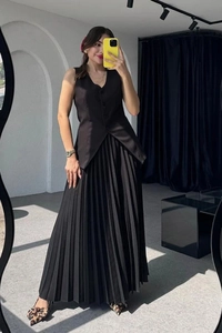 Damen Set mit schwarzer ärmelloser Weste und plissiertem Maxirock an einem Model vor Spiegel