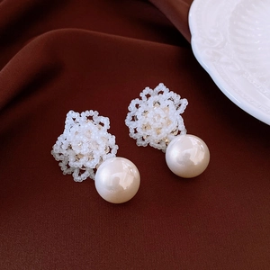 Close-up of white floral cluster pearl earrings with matte beads on brown velvet background