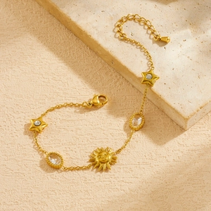 Detail of gold-plated sun and star charms on a stainless steel bracelet with stone texture