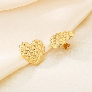 Macro detail of gold heart stud earrings with quilted pattern on cream satin fabric