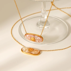 Detail of gold seashell pendant with pink resin flakes on a minimalist steel necklace