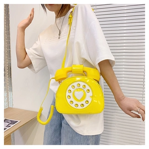 Detail of creative vintage telephone crossbody bag in bright yellow patent leather with handset