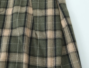 Vue macro du tissu à carreaux olive et café avec des détails plissés sur le pantalon