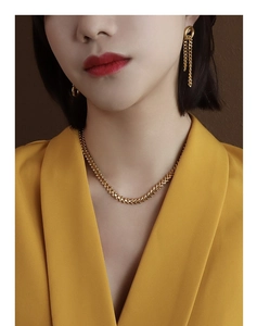 Detail view of gold leaf-textured necklace and tassel earrings on a model with yellow suit