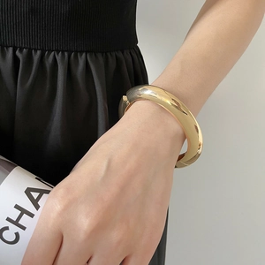 Détail d'un bracelet jonc doré épais au poignet avec un design moderne minimaliste