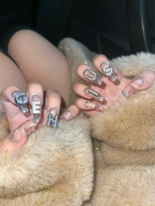 Detail of transparent long false nails with silver rhinestone letter G-E-N-U-S charms