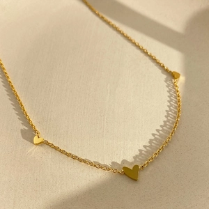 Elegante collar de acero de titanio dorado con pequeños dijes de corazones