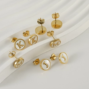 Detailed view of gold stainless steel initial earrings J K M with white shell inlay on white wave