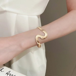 Detail of a minimalist gold wave cuff bracelet on model wrist with polished finish
