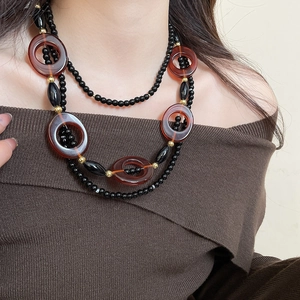 Detail view of double-layered black beaded necklace with reddish-brown ring pendants