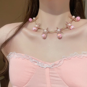 Close-up of golden choker necklace with pink rhinestone starfish and marble beads on model