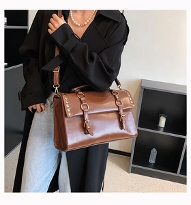 Brown vintage leather shoulder bag with buckle straps and studs worn by a model