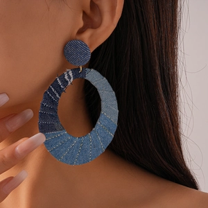 Close-up of model wearing oversized oval denim fabric hoop earrings with textured stitching