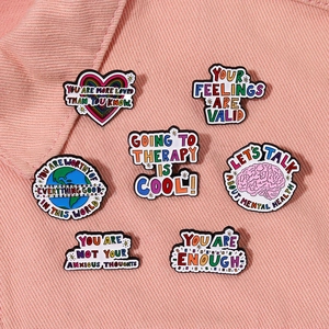 Set of 7 colorful mental health enamel pins with motivational quotes on pink denim fabric