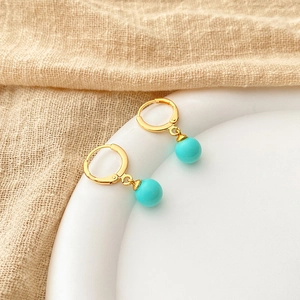 Detail of a 18K gold plated hoop earring featuring a turquoise blue pearl bead on a base