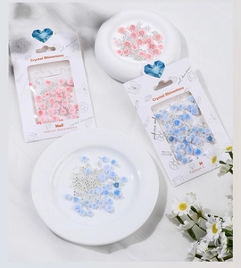 Detailed view of pink and blue resin rose nail charms with pearls in retail packaging