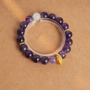 Detail of amethyst beaded bracelet with a white bead and embossed gold decorative ball