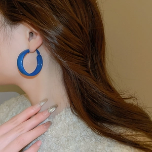 Close-up of a large Klein blue resin hoop earring worn on an ear with a cozy sweater