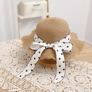Detail of hand-woven straw hat with scalloped brim and polka dot bow on lace tablecloth