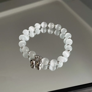 Detailansicht des Opal-Perlenarmbands mit Silberglöckchen auf reflektierender Spiegeloberfläche