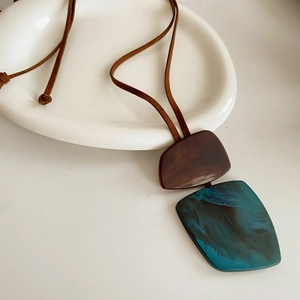 Macro shot of long necklace featuring brown leather cord and marble resin pendants