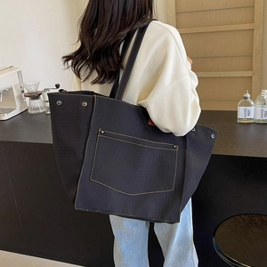Detail view of large black canvas tote bag featuring contrast stitching and metal rivets