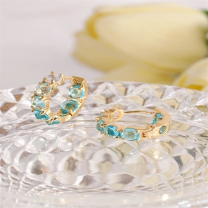 Elegant gold hoop earrings with light blue and clear oval zircons on glass base