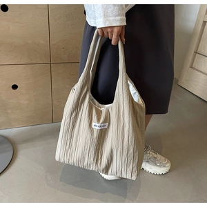 Beigefarbene Plissee-Tasche mit KISS YOURSELF Label am Model für Größe und Stil