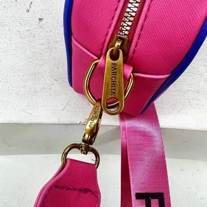 Detailed close-up of golden metal zipper and buckle on a pink textured shoulder bag